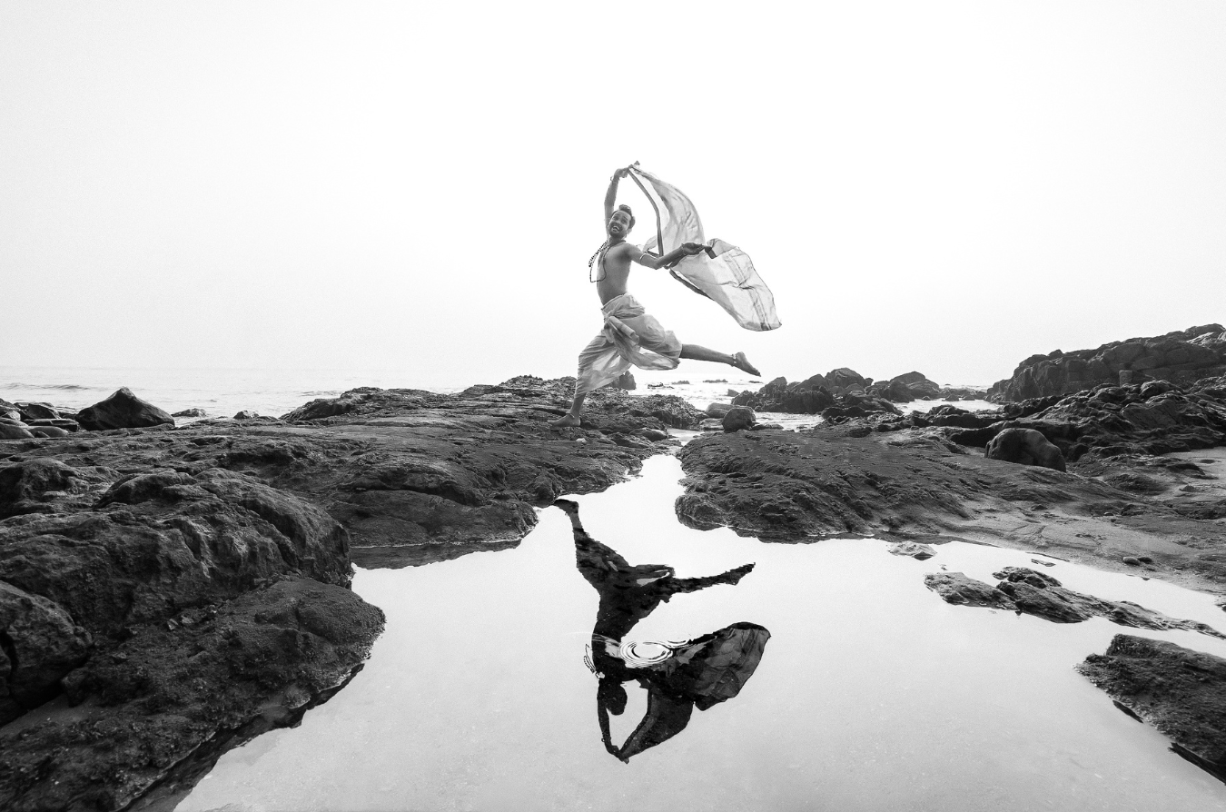 Uday Shenkar in mid-leap on the seashore, dhoti and shawl flowing in the wind
